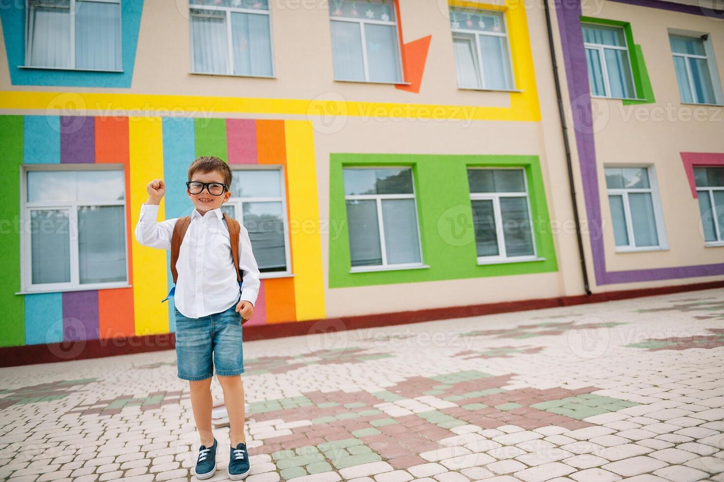 Back to school. Happy smiling boy in glasses is going to school for the first time. Child with backpack and book outdoors. Beginning of lessons. First day of fall photo