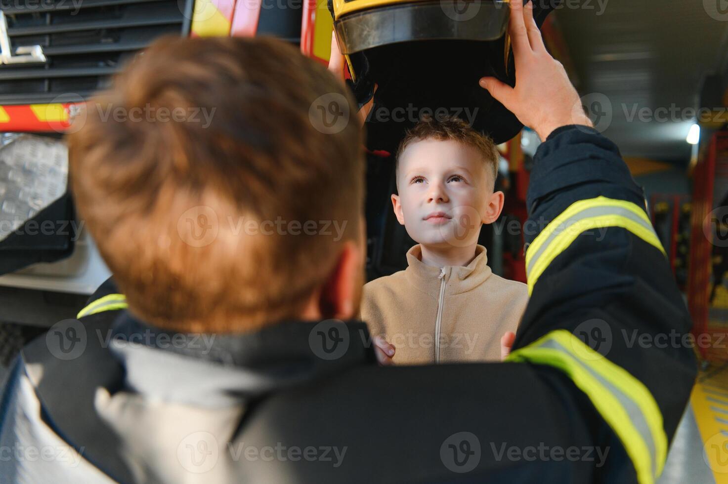 A fireman shows his work to his young son. A boy in a firefighter's helmet photo