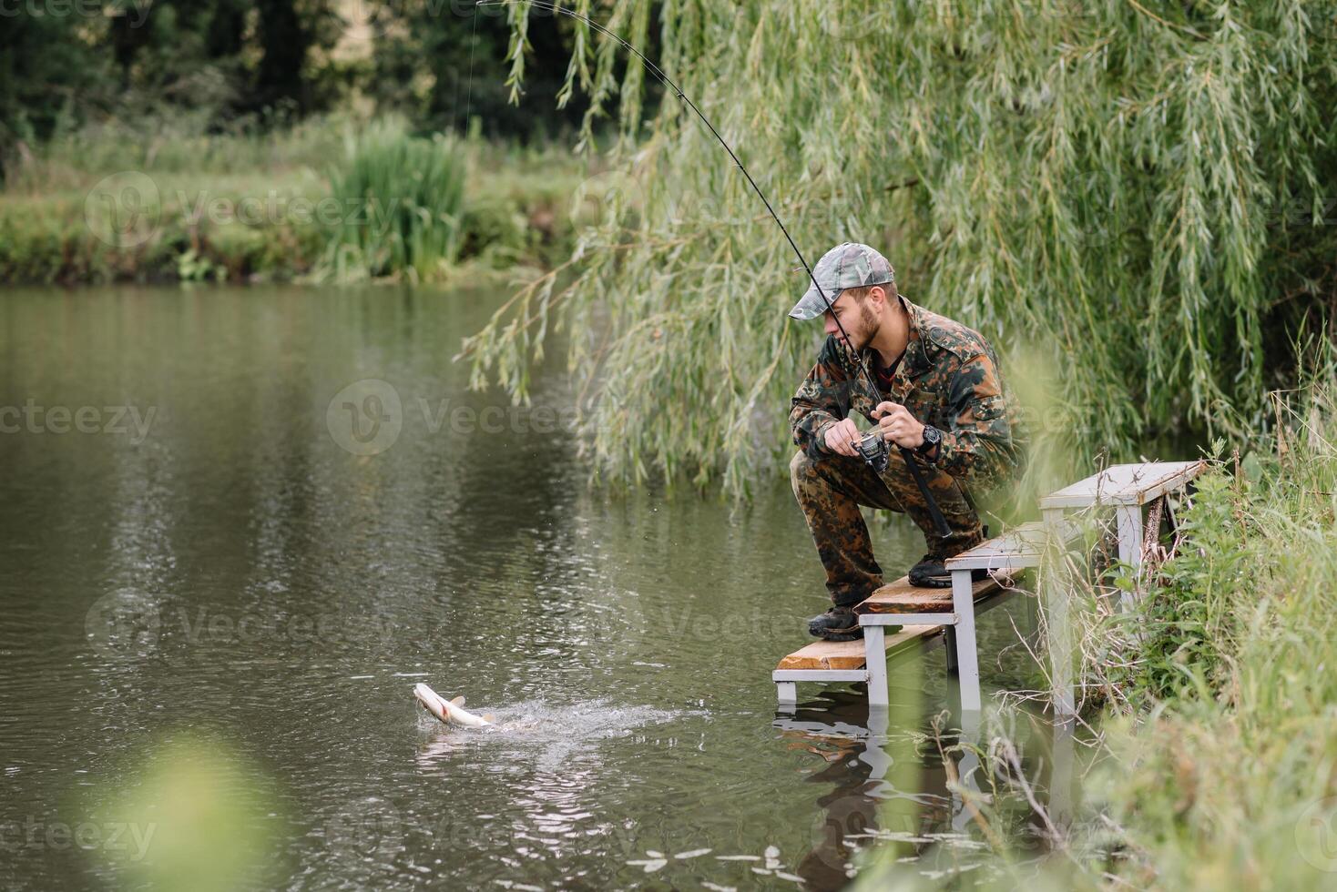 pescar en rio.a pescador con un pescar varilla en el río banco. hombre pescador capturas un pescado pesca del lucio, hilado carrete, pez, breg ríos - el concepto de un rural escapar. artículo acerca de pescar foto