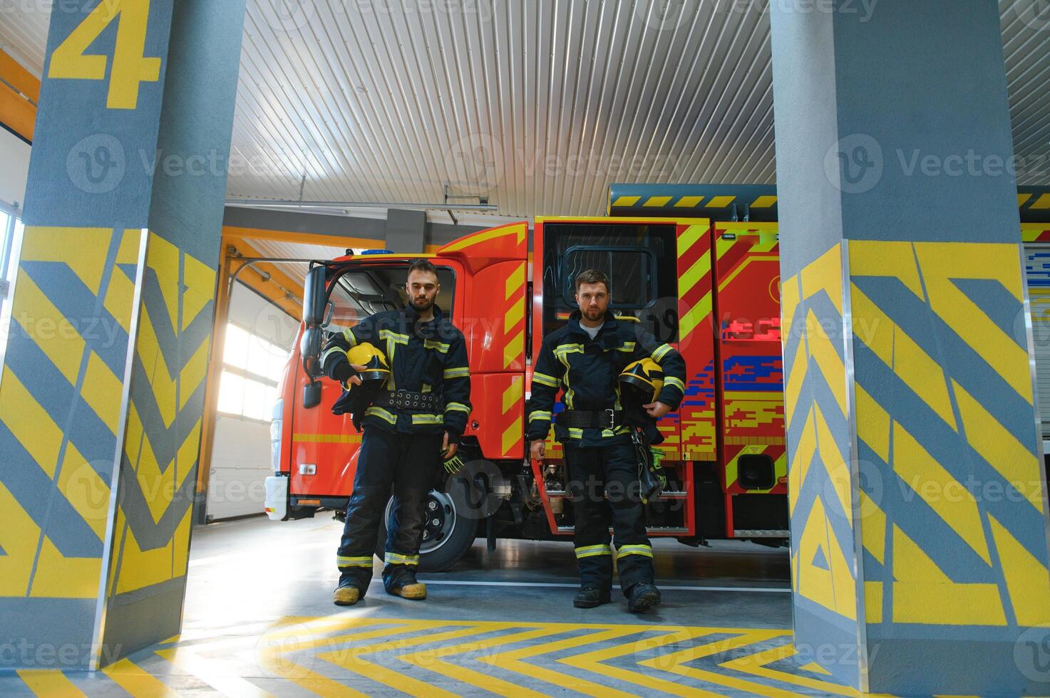 Portrait of two young firemen in uniform standing inside the fire station photo