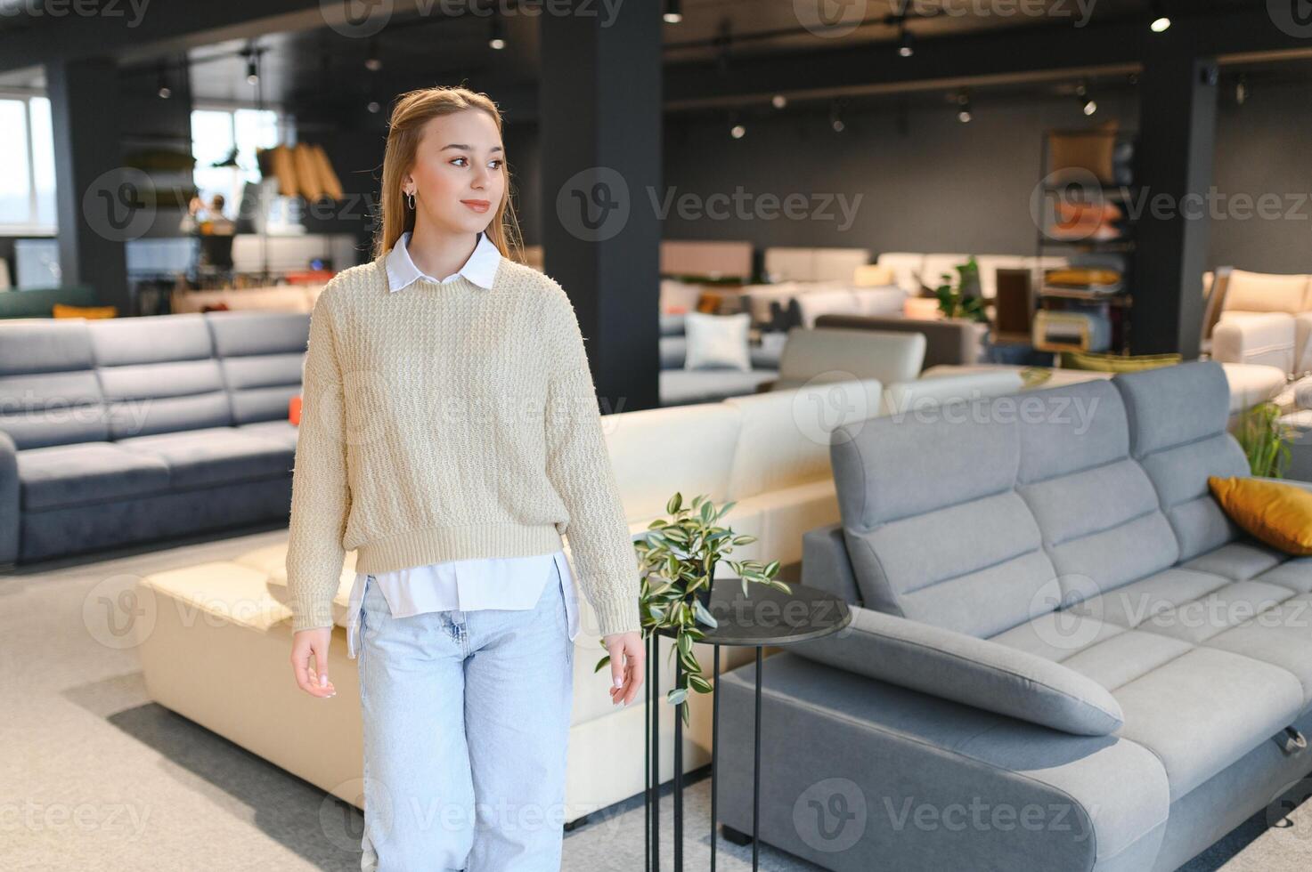 Portrait of young cheerful woman testing sofa in furniture store photo