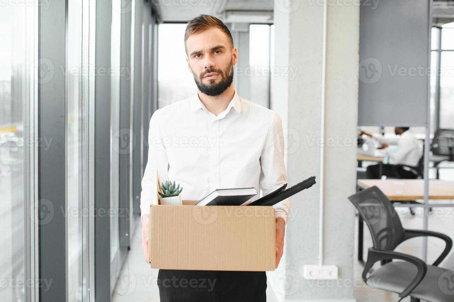 joven hermoso empresario en ligero moderno oficina con caja de cartón caja. último día a trabajar. trastornado oficina trabajador es despedido foto