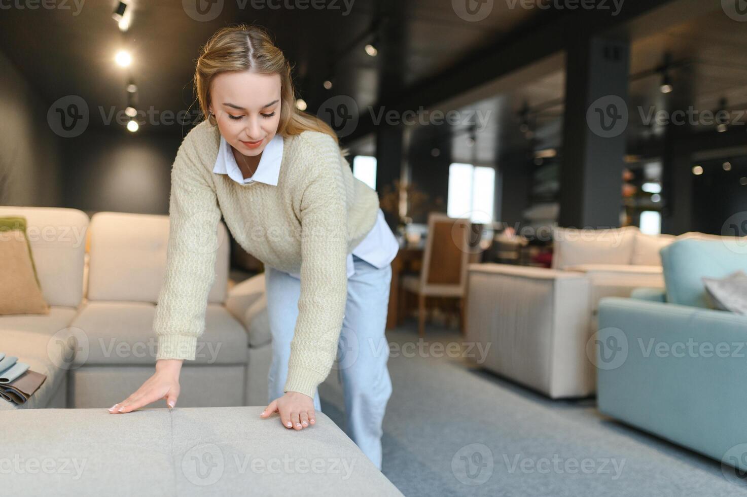 Portrait of young cheerful woman testing sofa in furniture store photo