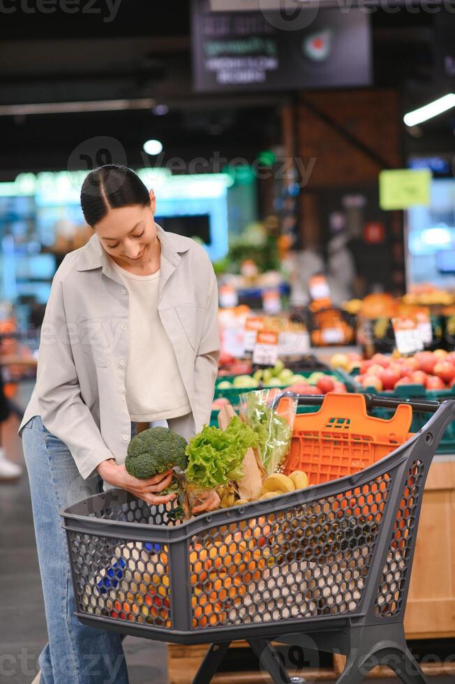 Young woman chooses broccoli, buying vegetables in supermarket. photo