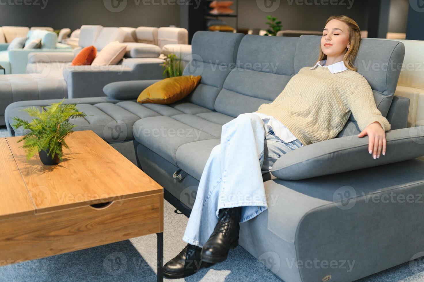 Happy young woman chooses sofa for home in furniture store photo