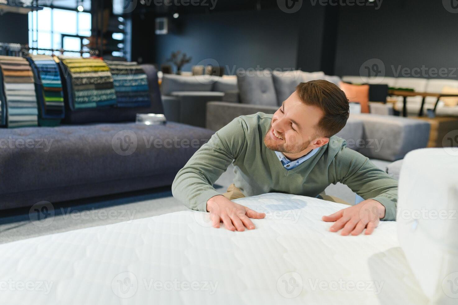 Young male customer examining orthopedic mattress on sale at furniture store, copy space photo