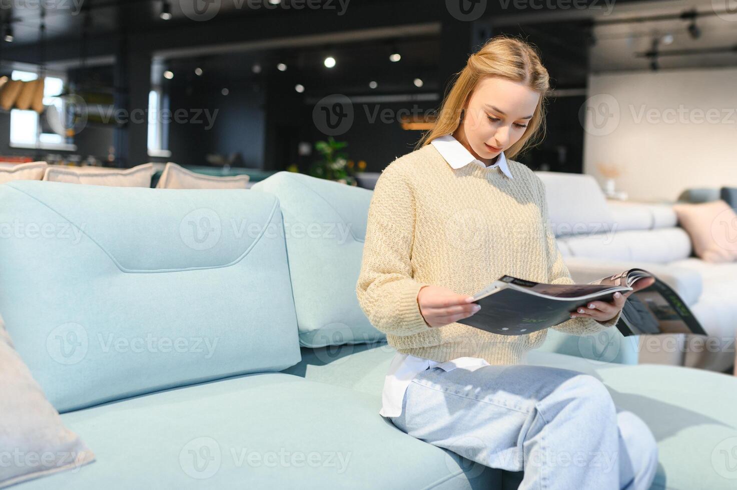 Portrait of young cheerful woman testing sofa in furniture store photo