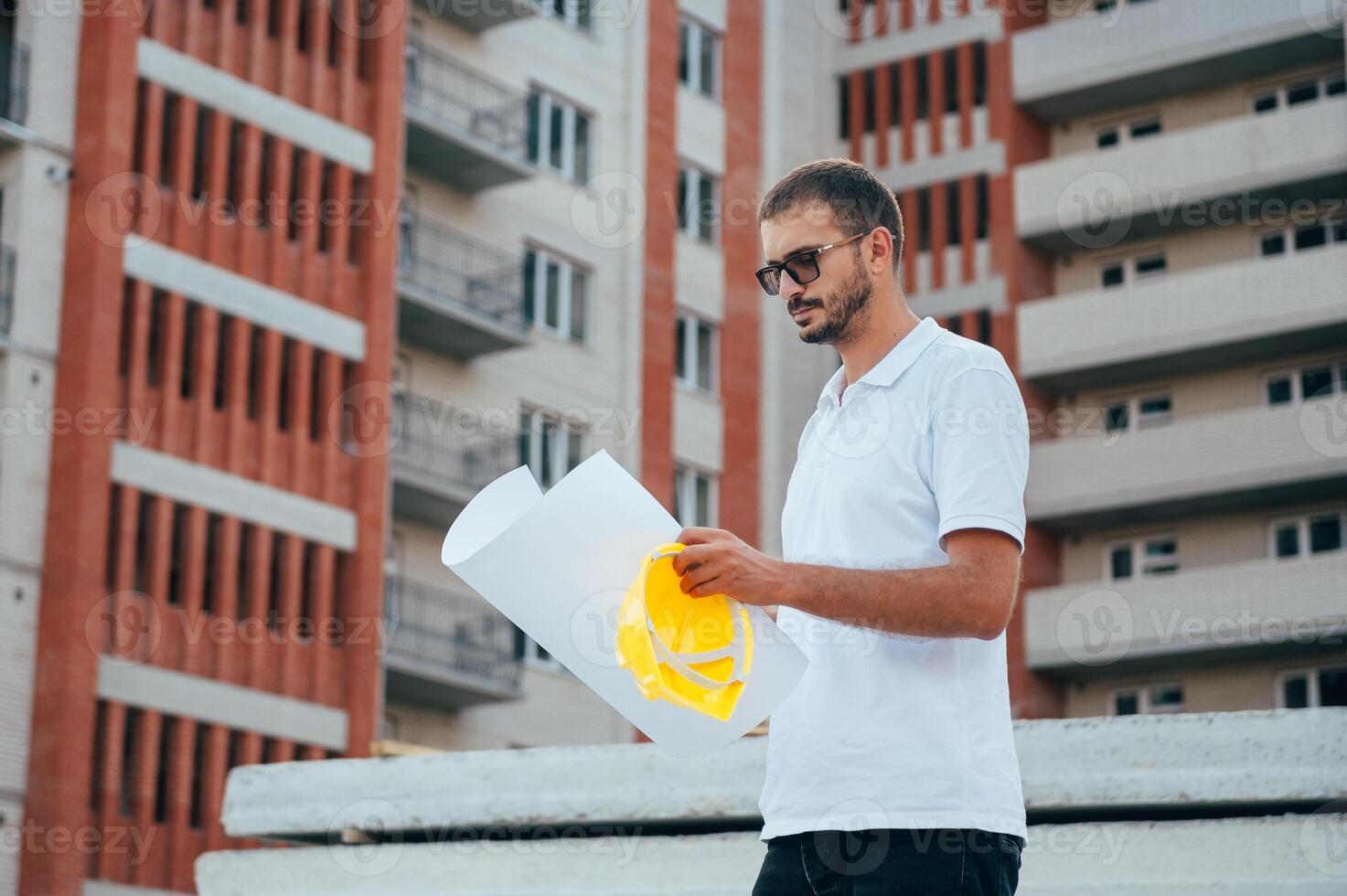 Portrait of an architect builder studying layout plan of the rooms, serious civil engineer working with documents on construction site. photo