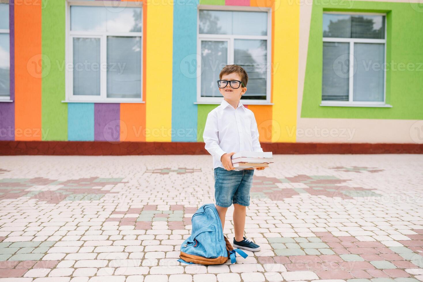 Back to school. Happy smiling boy in glasses is going to school for the first time. Child with backpack and book outdoors. Beginning of lessons. First day of fall photo