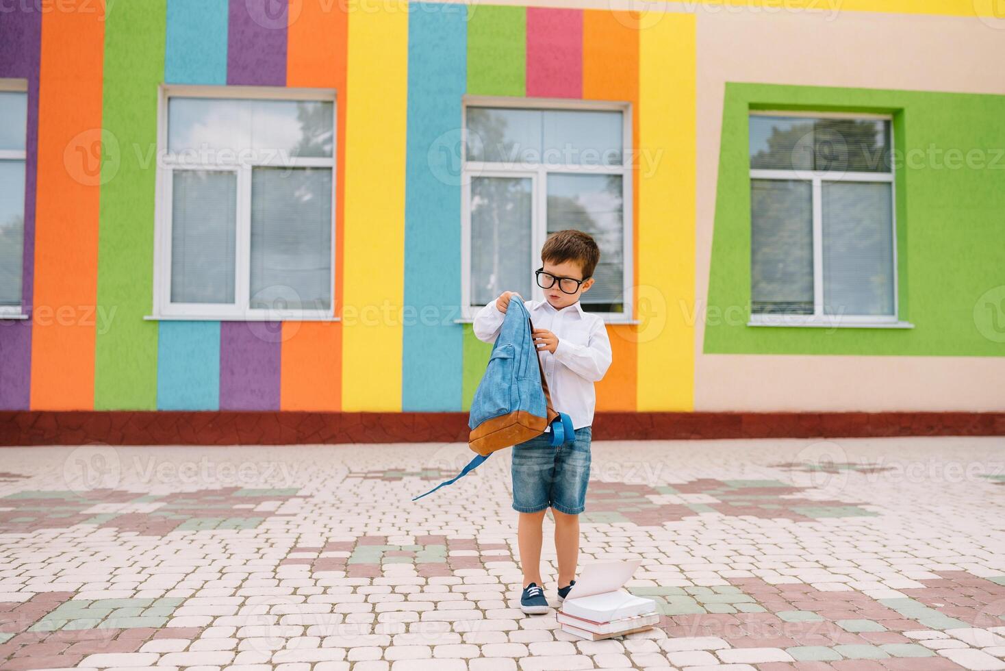 Back to school. Happy smiling boy in glasses is going to school for the first time. Child with backpack and book outdoors. Beginning of lessons. First day of fall. photo