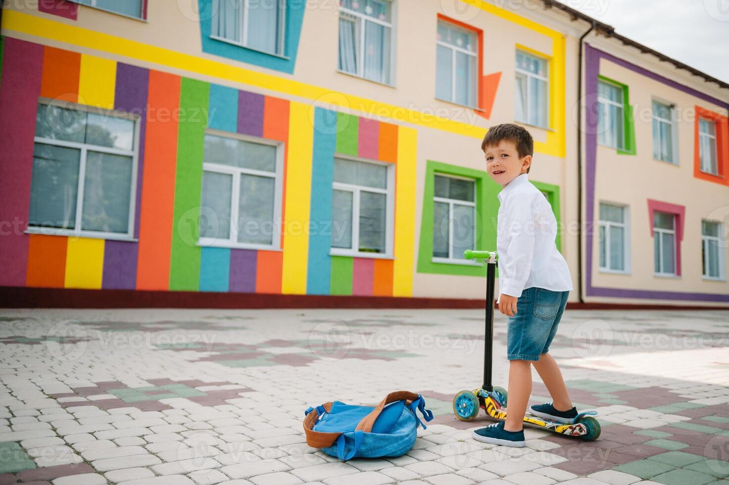 Teenage boy with kick scooter near modern school. Child with backpack and book outdoors. Beginning of lessons. First day of fall. Back to school. photo