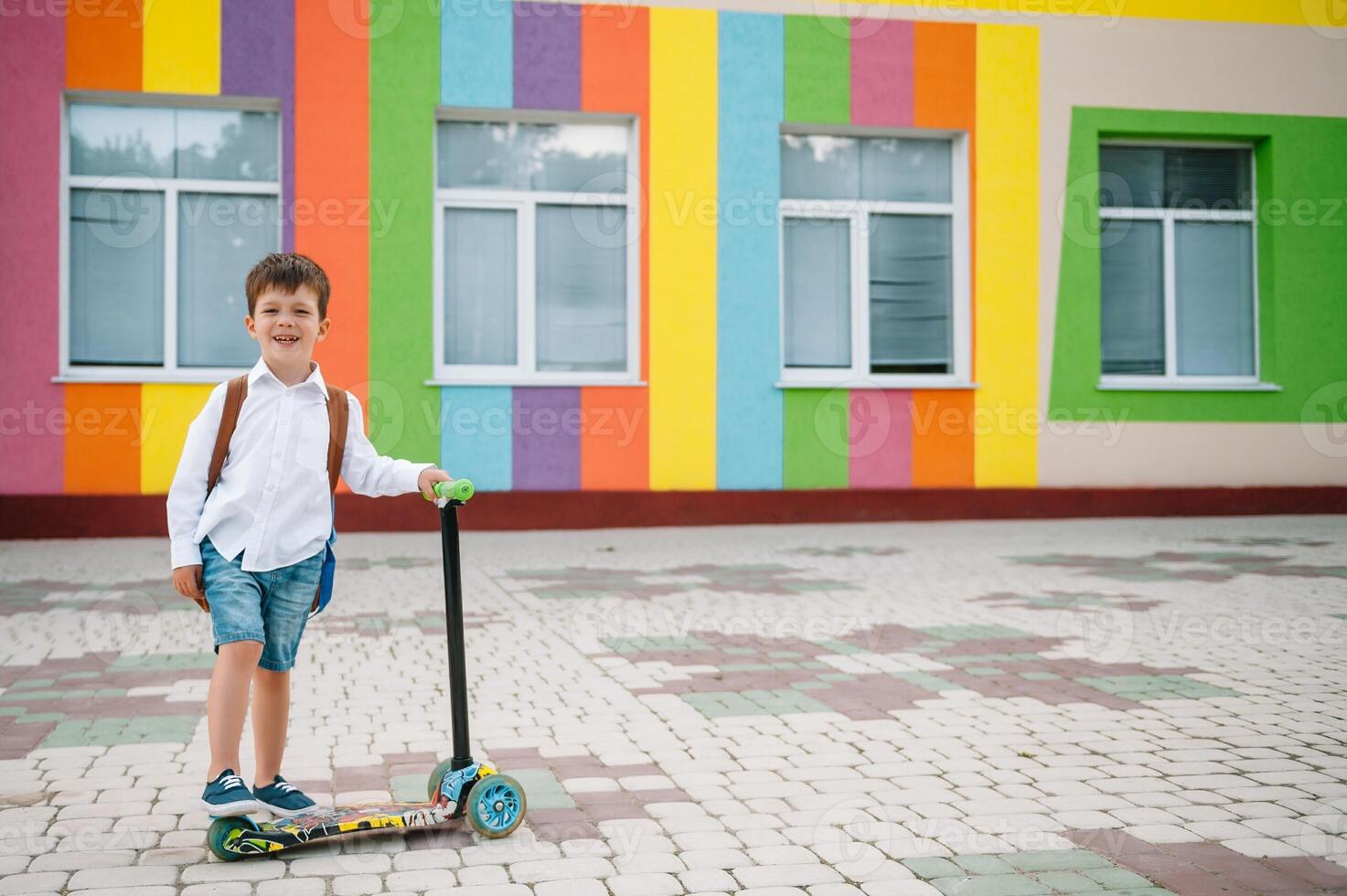 Teenage boy with kick scooter near modern school. Child with backpack and book outdoors. Beginning of lessons. First day of fall. Back to school. photo