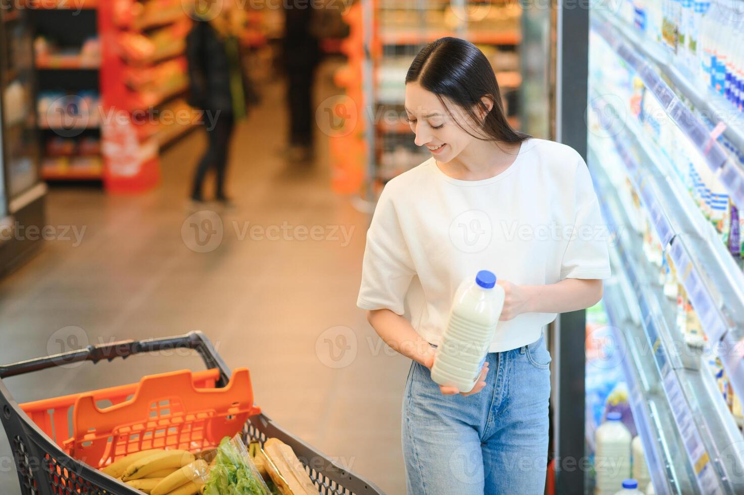 sonriente contento mujer disfrutando compras a el supermercado, ella es propensión en un lleno carro foto