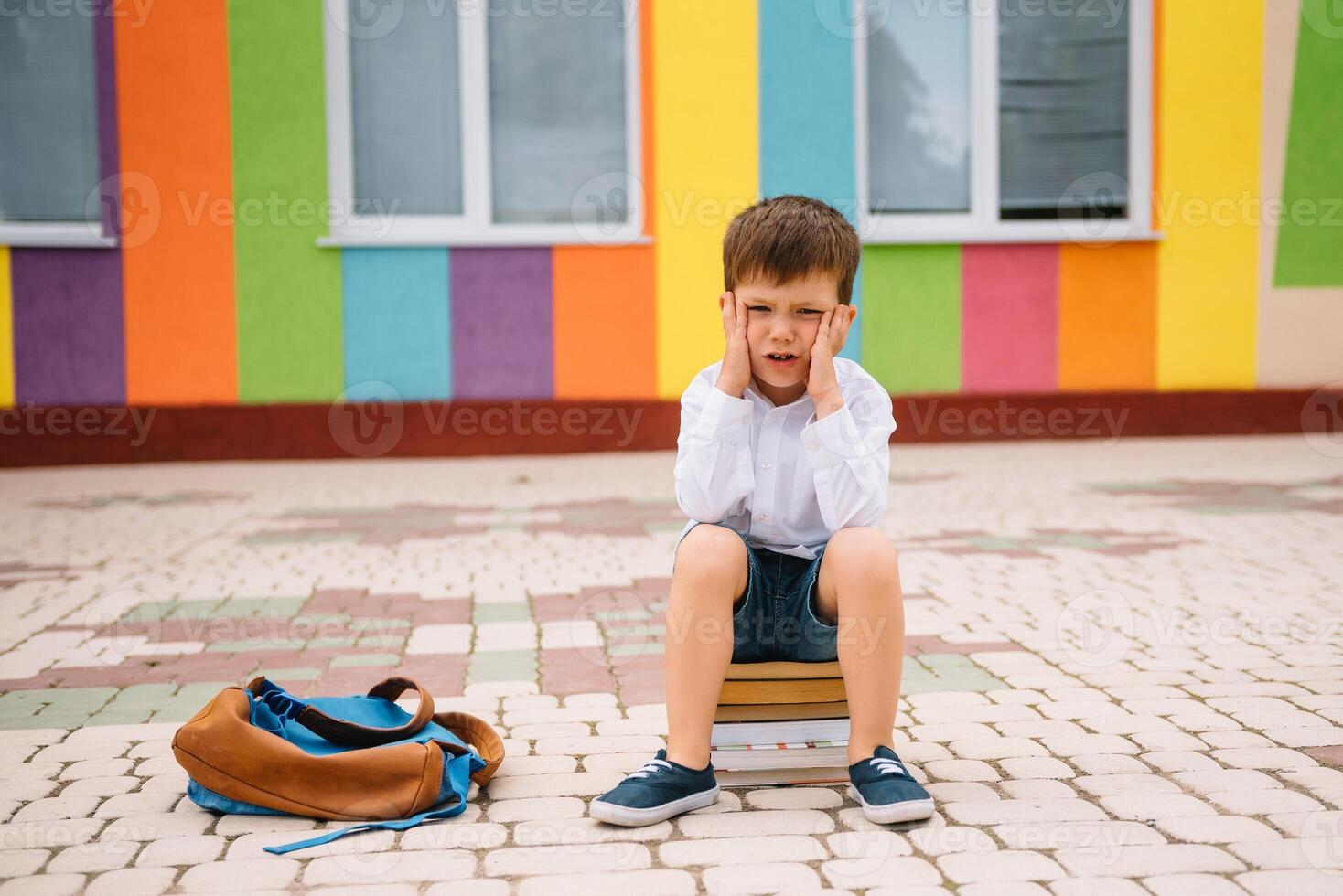 triste pequeño chico fuera de de escuela. triste colegial con libros cerca un moderno escuela. colegio concepto. espalda a escuela. foto