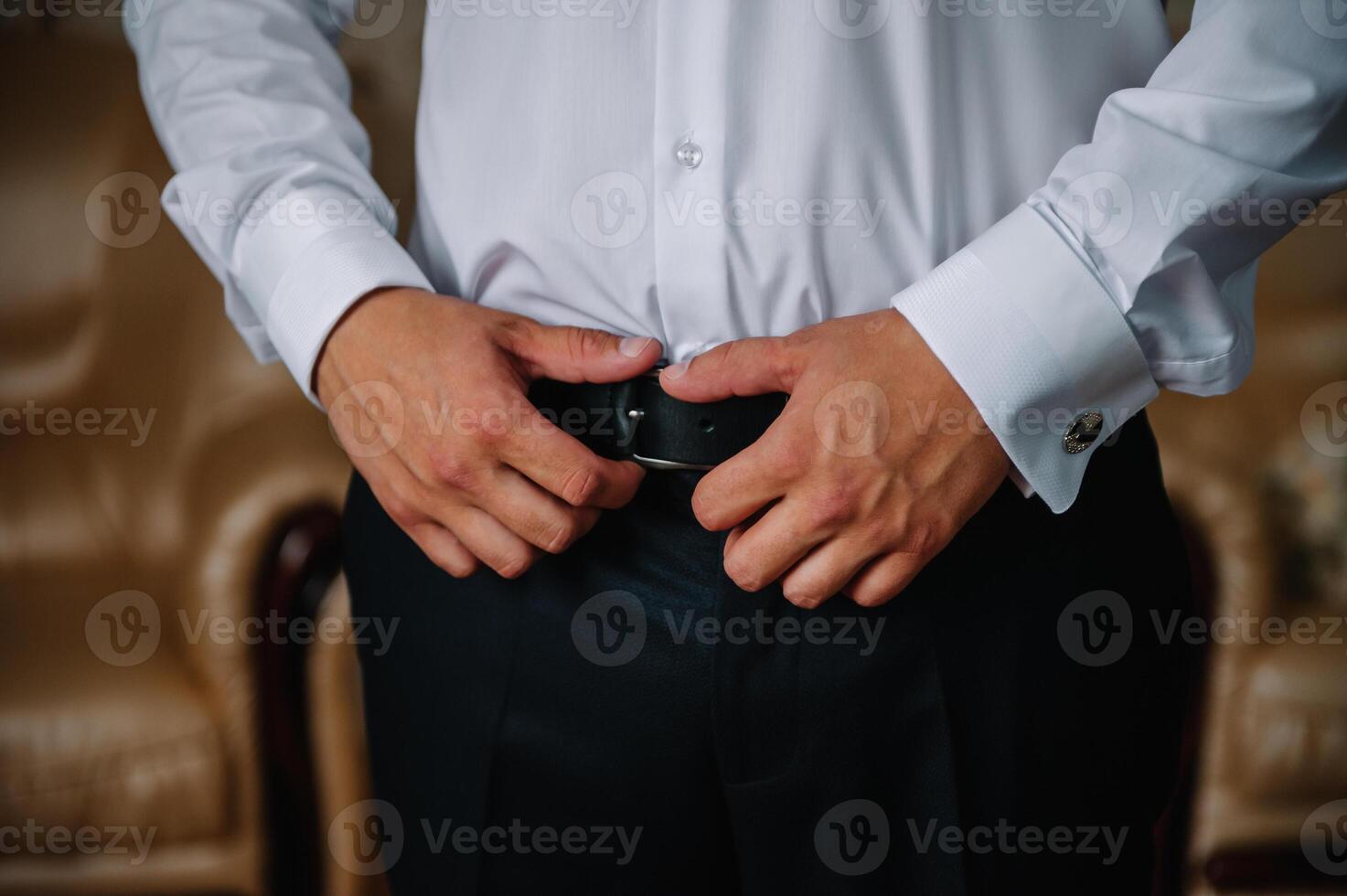 un hombre en azul pantalones y un blanco camisa abotonado un marrón cuero pantalón cinturón. él tiene un reloj en su mano foto