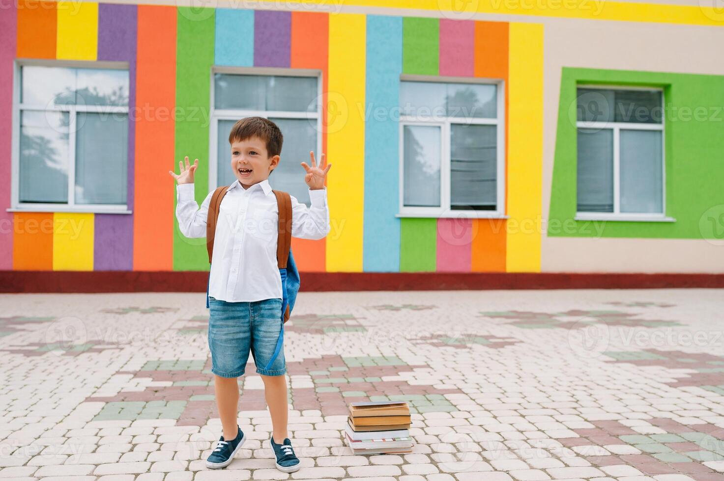 Back to school. Happy smiling boy in glasses is going to school for the first time. Child with backpack and book outdoors. Beginning of lessons. First day of fall photo