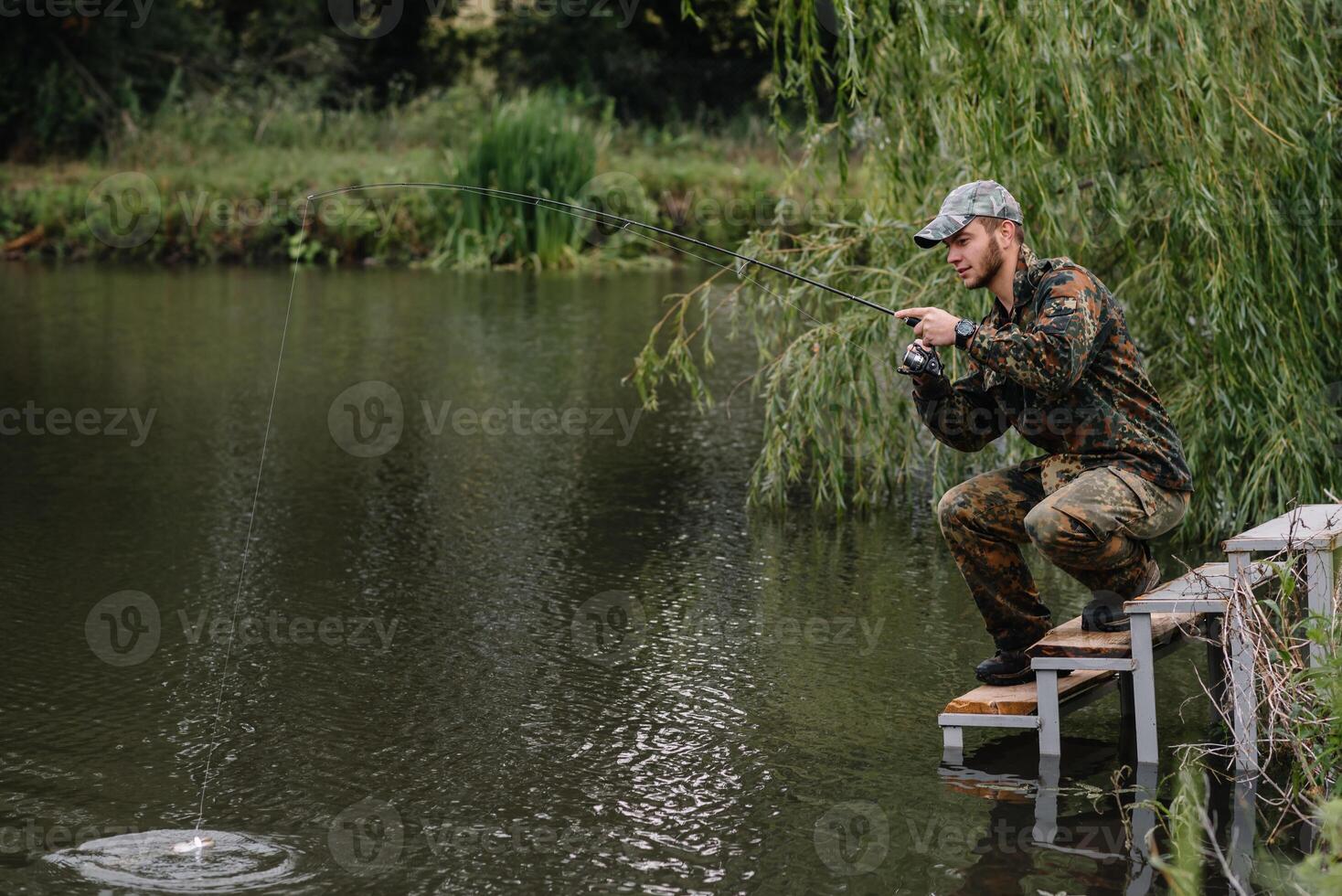 Fishing in river.A fisherman with a fishing rod on the river bank. Man fisherman catches a fish pike.Fishing, spinning reel, fish, Breg rivers. - The concept of a rural getaway. Article about fishing photo