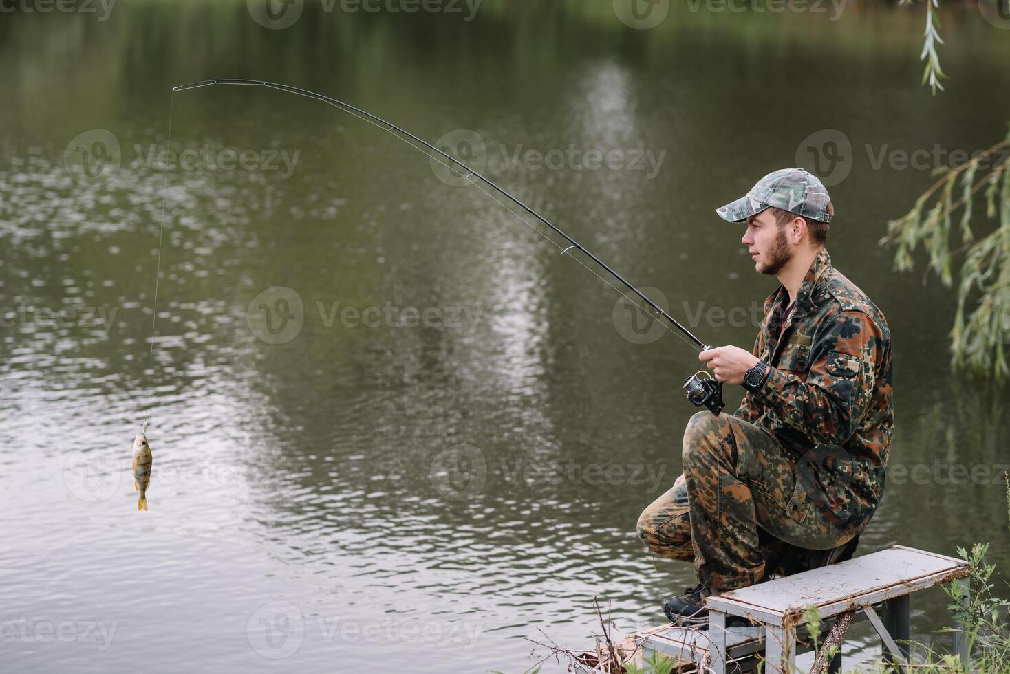 pescar en rio.a pescador con un pescar varilla en el río banco. hombre pescador capturas un pescado pesca del lucio, hilado carrete, pez, breg ríos - el concepto de un rural escapar. artículo acerca de pescar foto