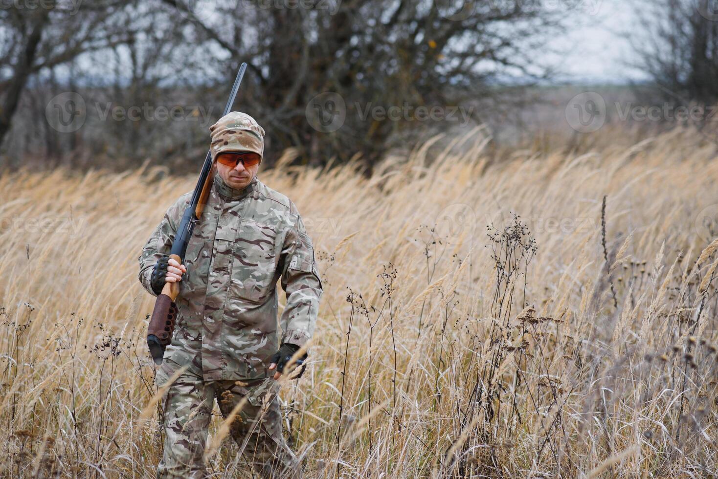 A male hunter with a gun while sitting takes aim at a forest. The concept of a successful hunt, an experienced hunter. Hunting the autumn season. The hunter has a rifle and a hunting uniform photo