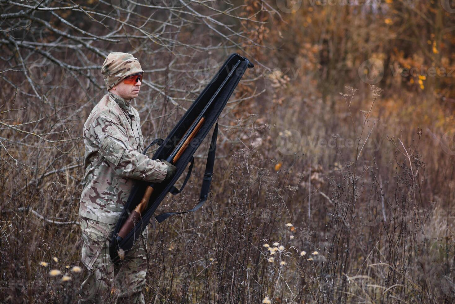 A male hunter with a gun while sitting takes aim at a forest. The concept of a successful hunt, an experienced hunter. Hunting the autumn season. The hunter has a rifle and a hunting uniform photo