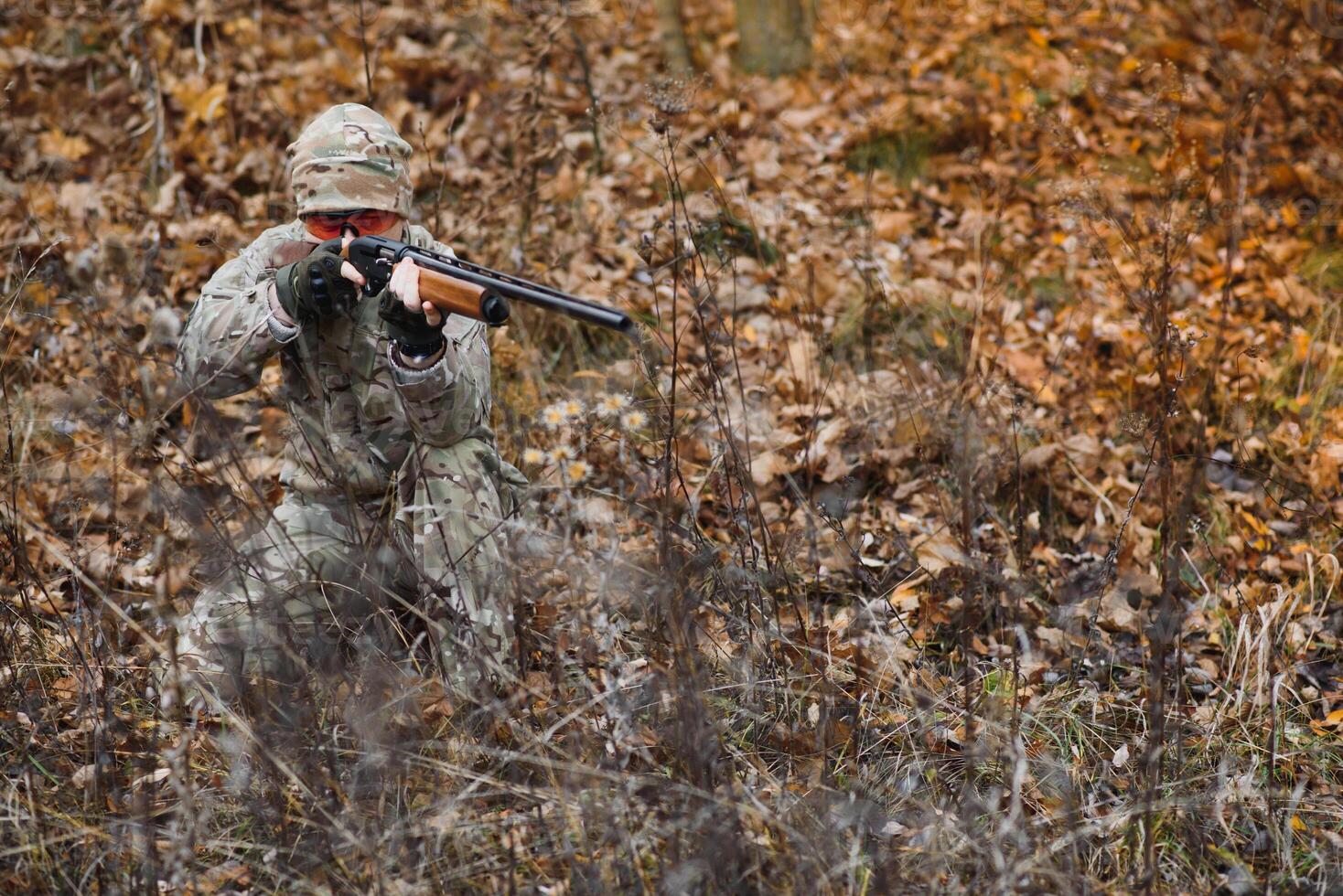 A male hunter with a gun while sitting takes aim at a forest. The concept of a successful hunt, an experienced hunter. Hunting the autumn season. The hunter has a rifle and a hunting uniform. photo