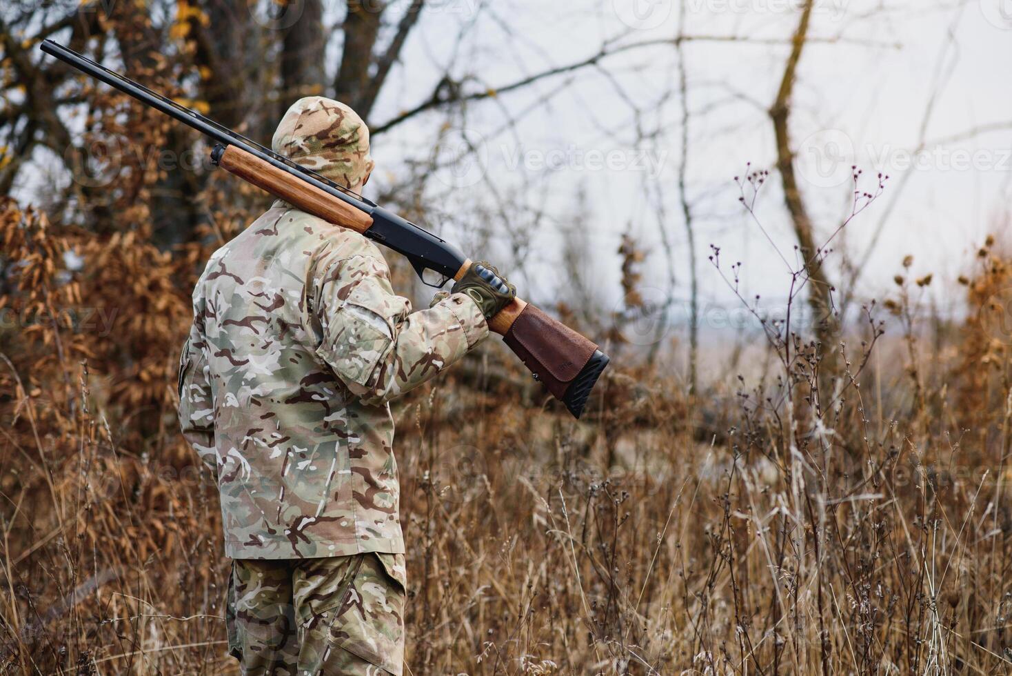 hunting, war, army and people concept - young soldier, ranger or hunter with gun walking in forest. photo