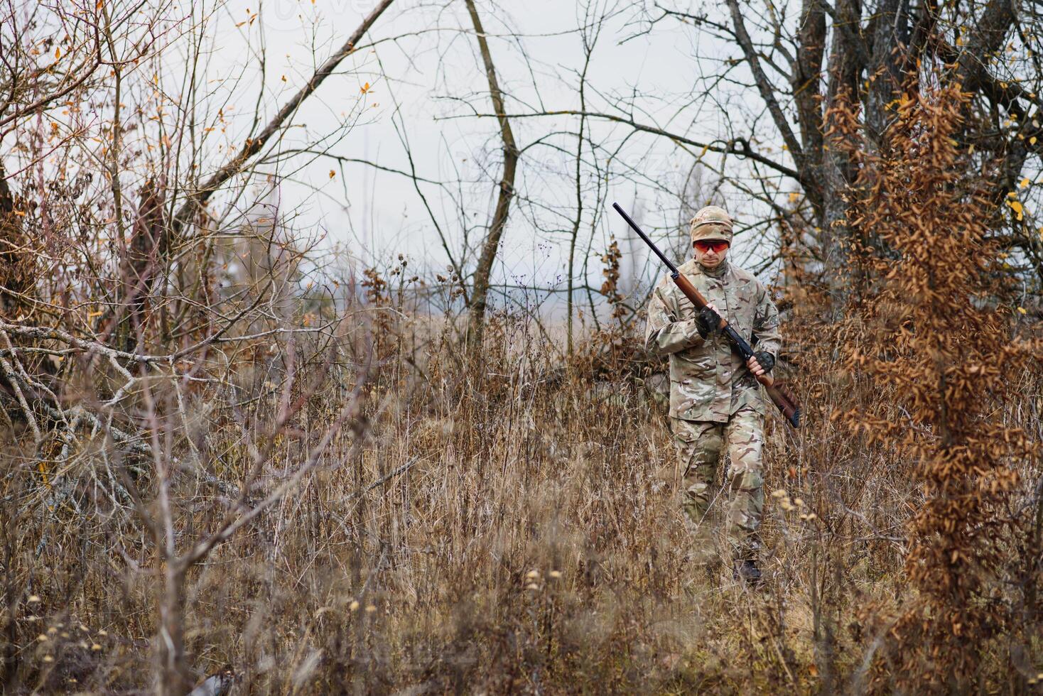 hunting, war, army and people concept - young soldier, ranger or hunter with gun walking in forest. photo