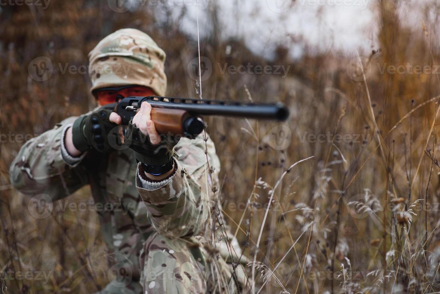 A male hunter with a gun while sitting takes aim at a forest. The concept of a successful hunt, an experienced hunter. Hunting the autumn season. The hunter has a rifle and a hunting uniform photo