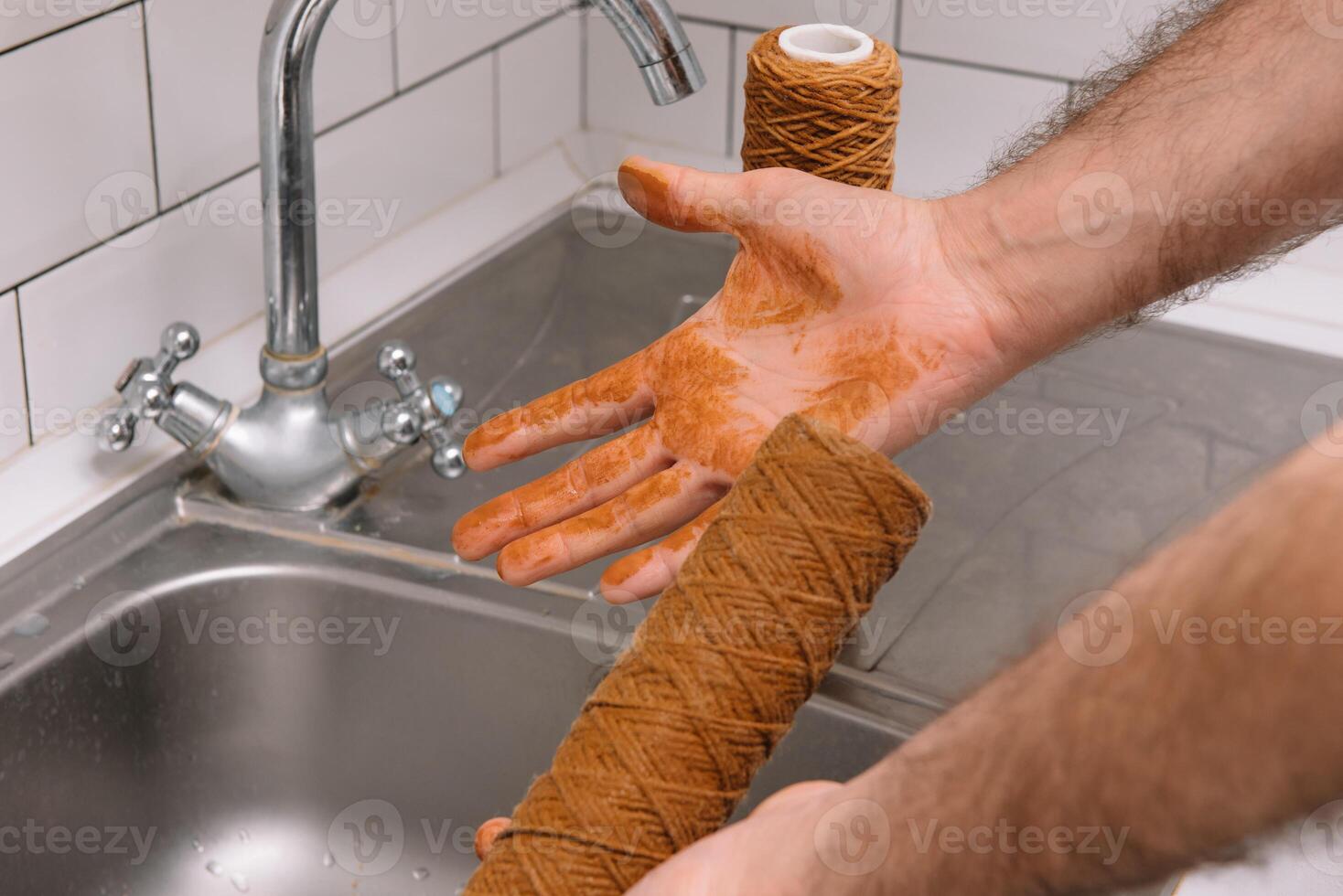 Hand holding dirty water filter cartridge over the sink. Brown coloring. Evidence of contamination of tap water with iron cations photo