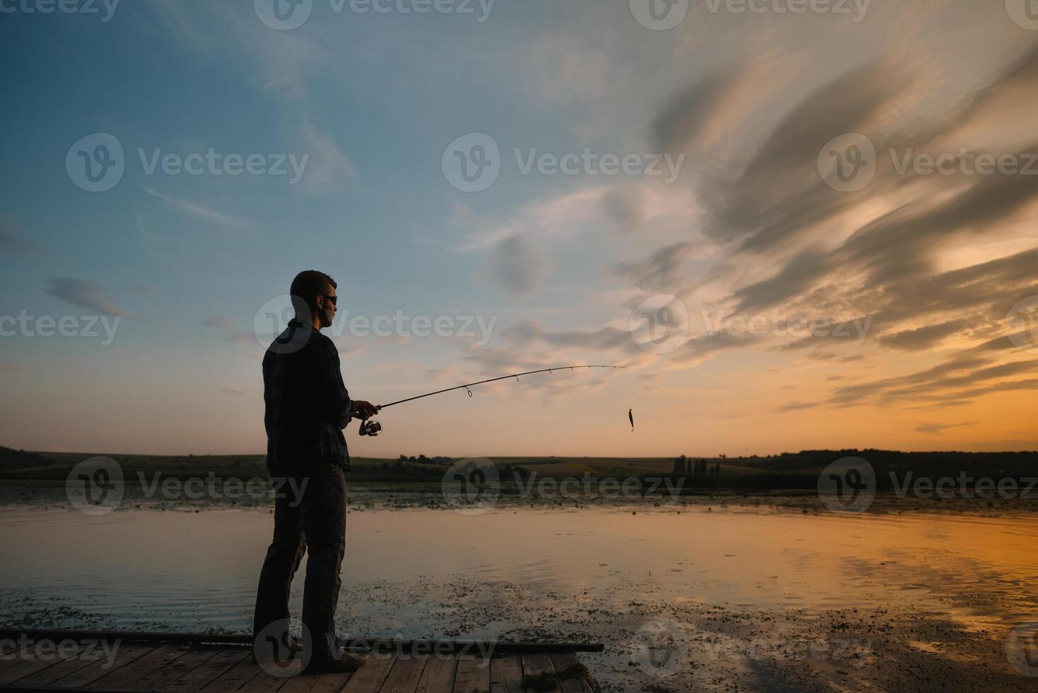 A fisherman silhouette fishing at sunset. Freshwater fishing, catch of fish. photo