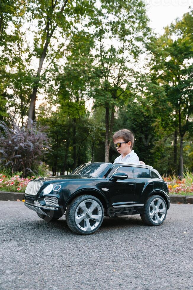 Cute boy in riding a black electric car in the park. Funny boy rides on a toy electric car. Copy space. photo