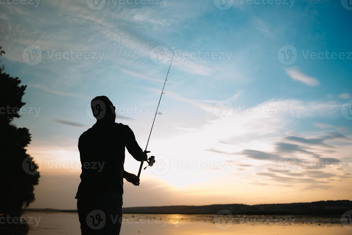 Fisher man fishing with spinning rod on a river bank at misty foggy sunrise. fisher with spinning. spinning concept. photo