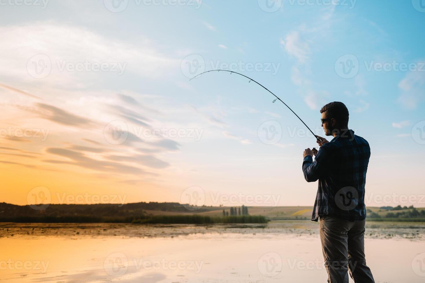 Fisher man fishing with spinning rod on a river bank at misty foggy sunrise. fisher with spinning. spinning concept. photo