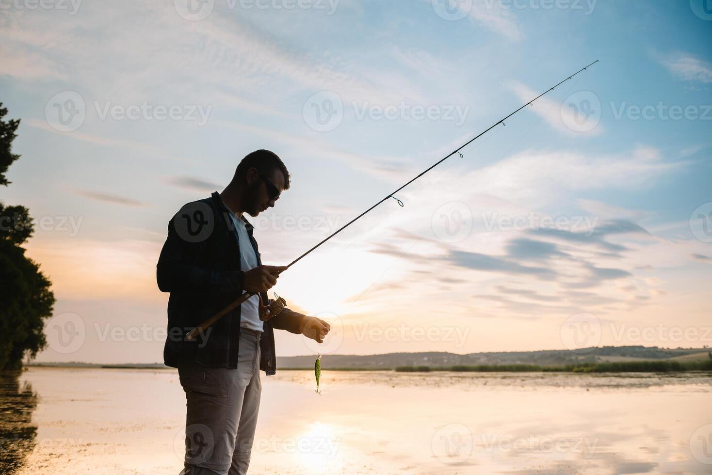 Fisher man fishing with spinning rod on a river bank at misty foggy sunrise. fisher with spinning. spinning concept. photo