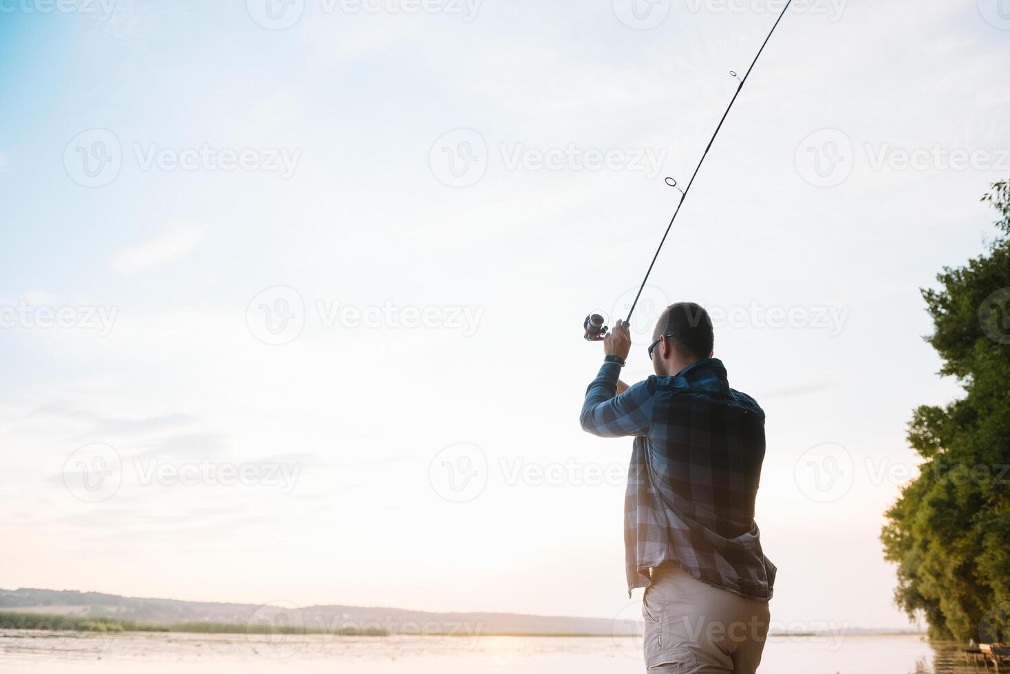 Fisher man fishing with spinning rod on a river bank at misty foggy sunrise. fisher with spinning. spinning concept. photo