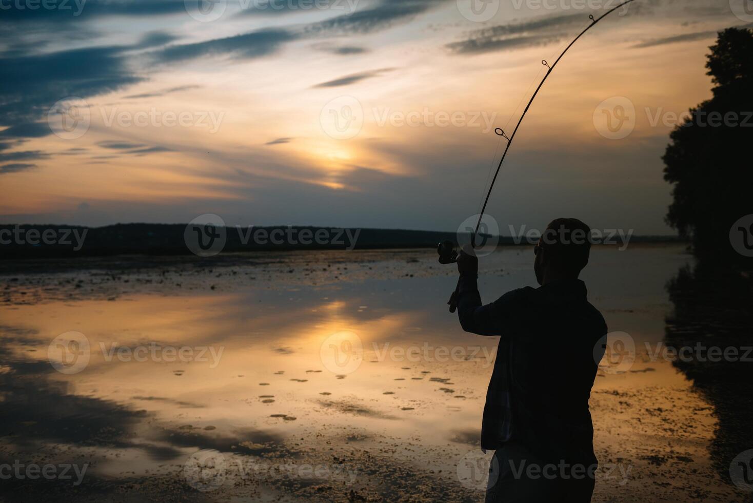 Fisher man fishing with spinning rod on a river bank at misty foggy sunrise. fisher with spinning. spinning concept. photo