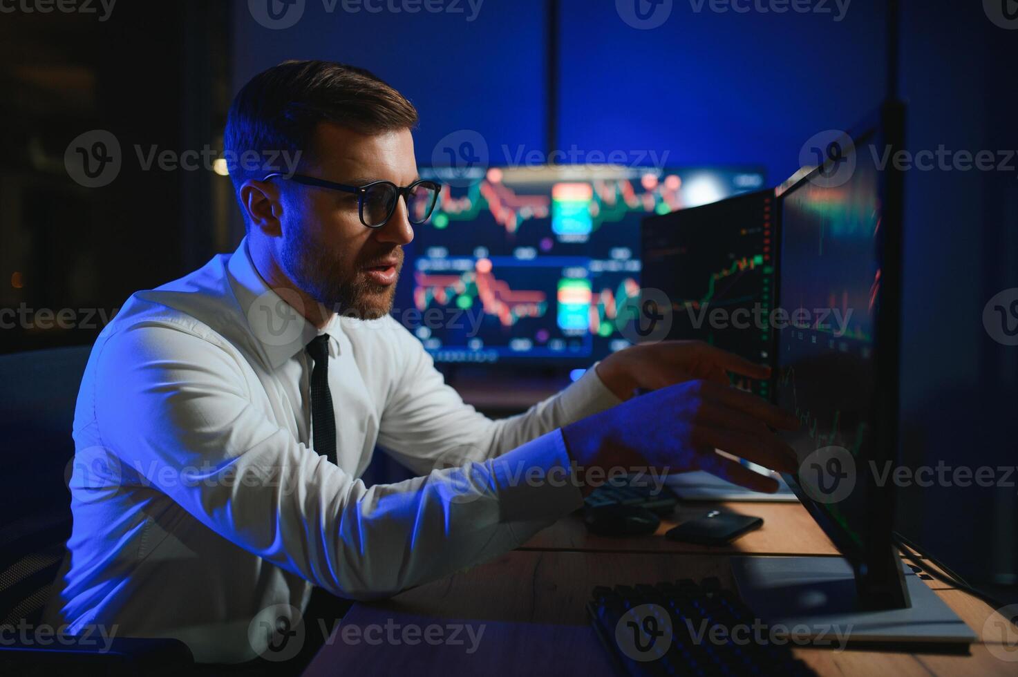 Side view of crypto broker sitting at office table, analyzing market, looking at screen photo