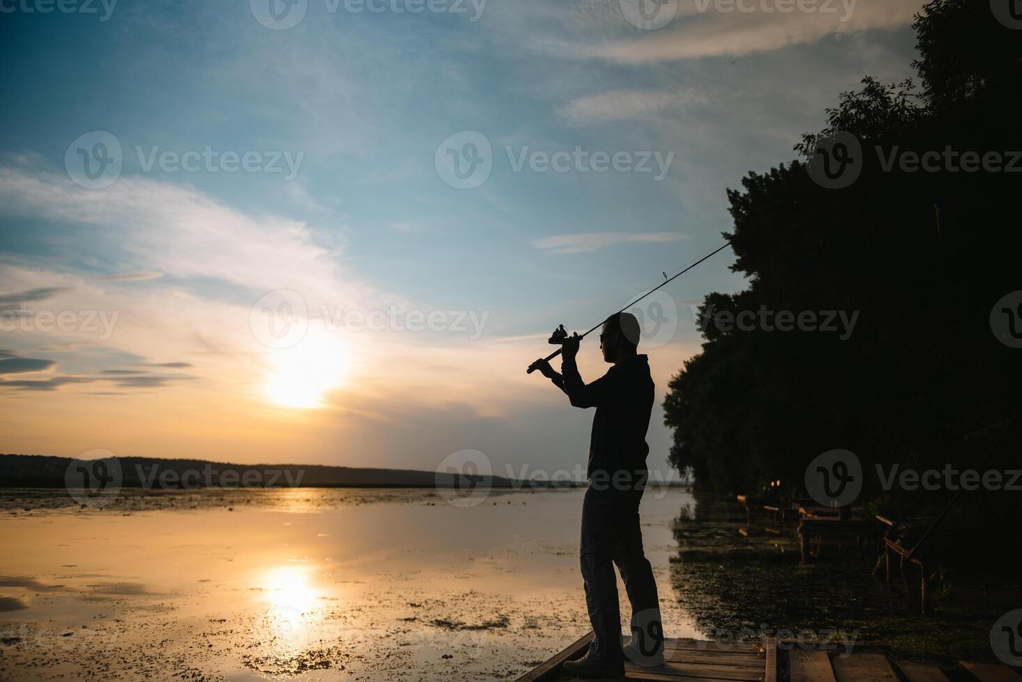 Fisherman at sunset on the river .Beautiful summer landscape with sunset on the river. Fishing. spinning at sunset. Silhouette of a fisherman. photo