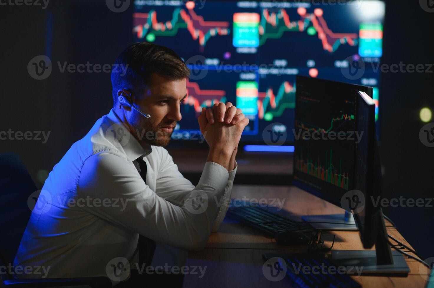 Side view of crypto broker sitting at office table, analyzing market, looking at screen photo