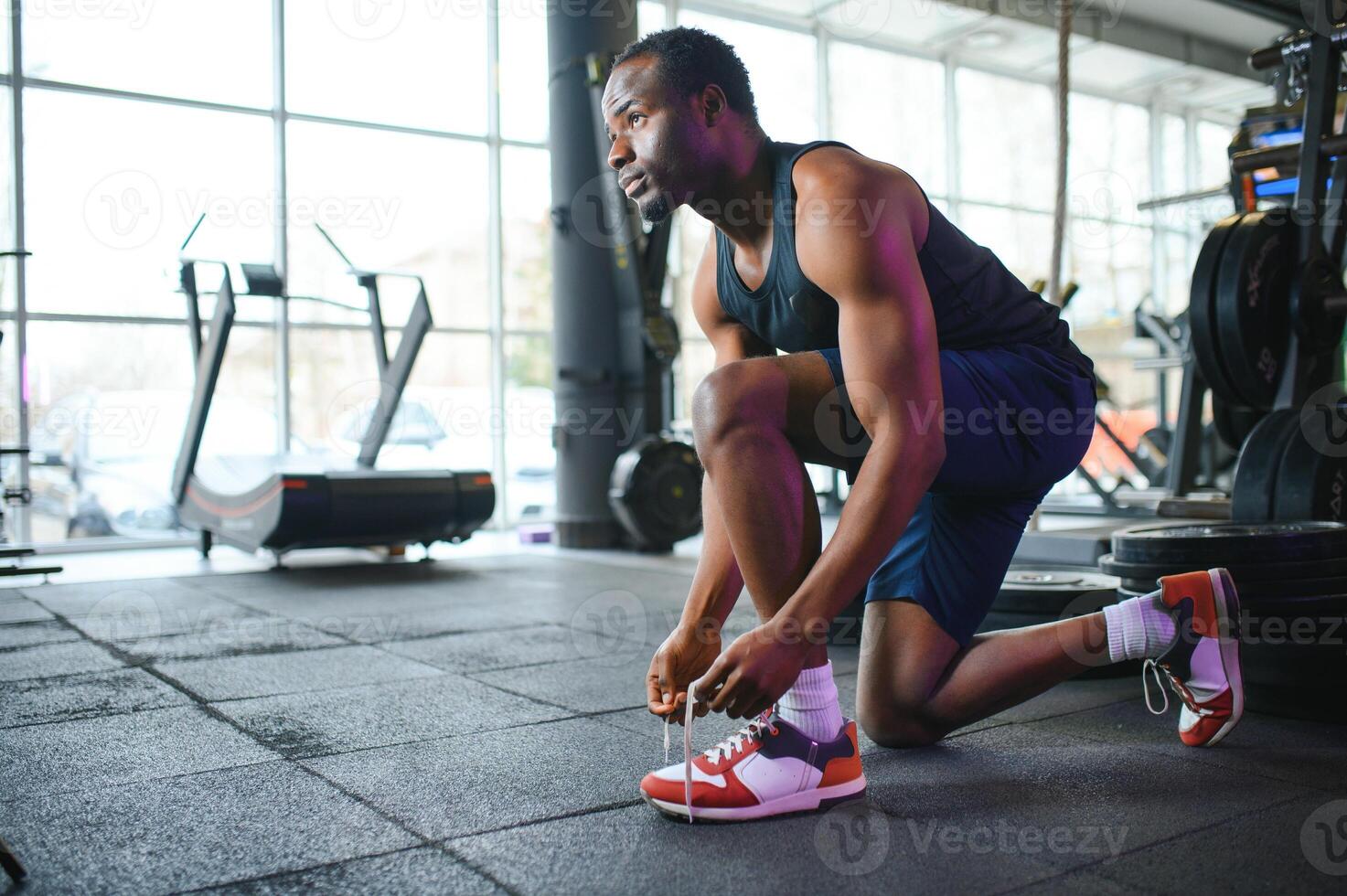 africano hombre atadura cordones de los zapatos a zapatilla de deporte en el gimnasio foto
