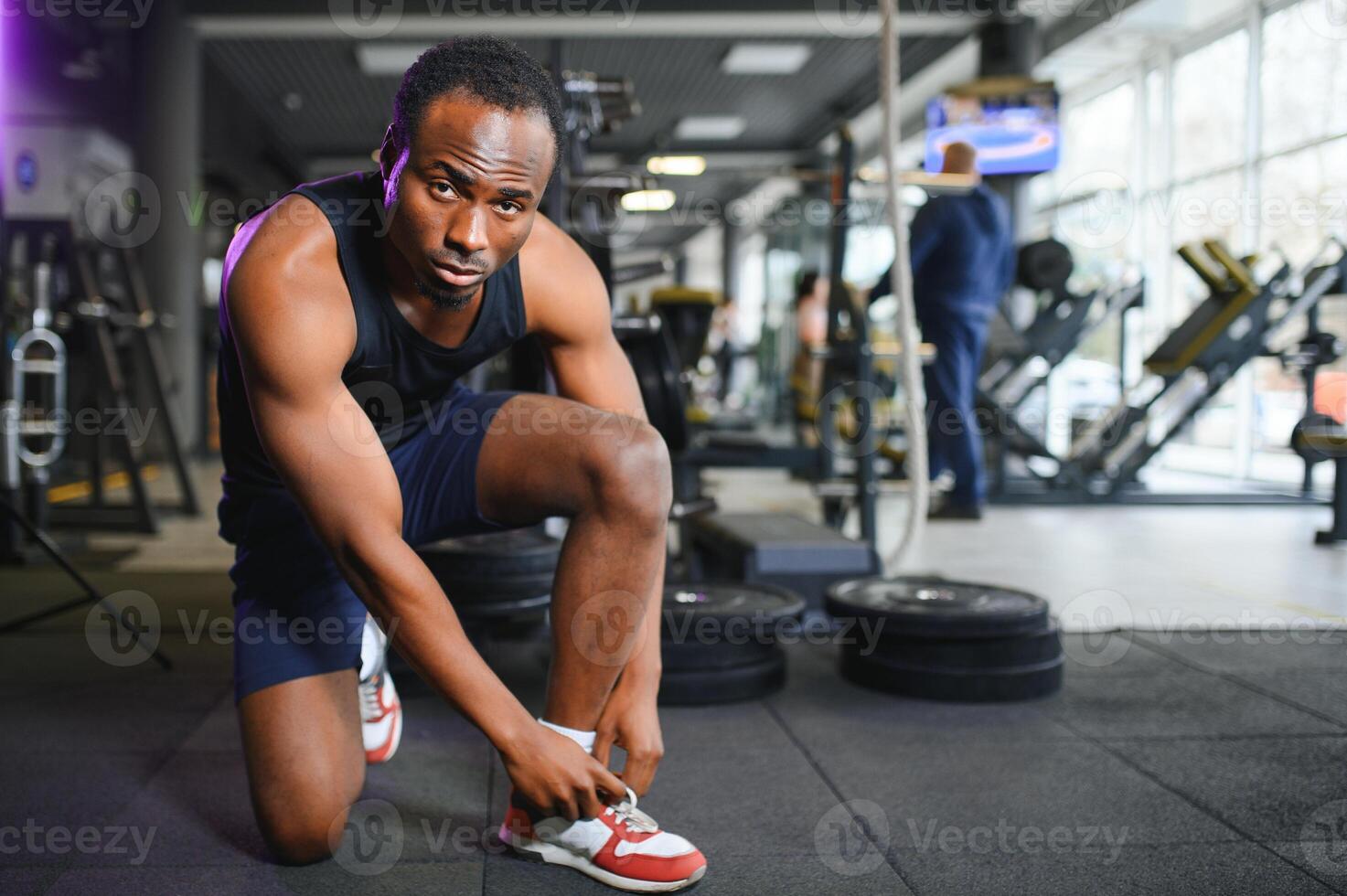 africano hombre atadura cordones de los zapatos a zapatilla de deporte en el gimnasio foto