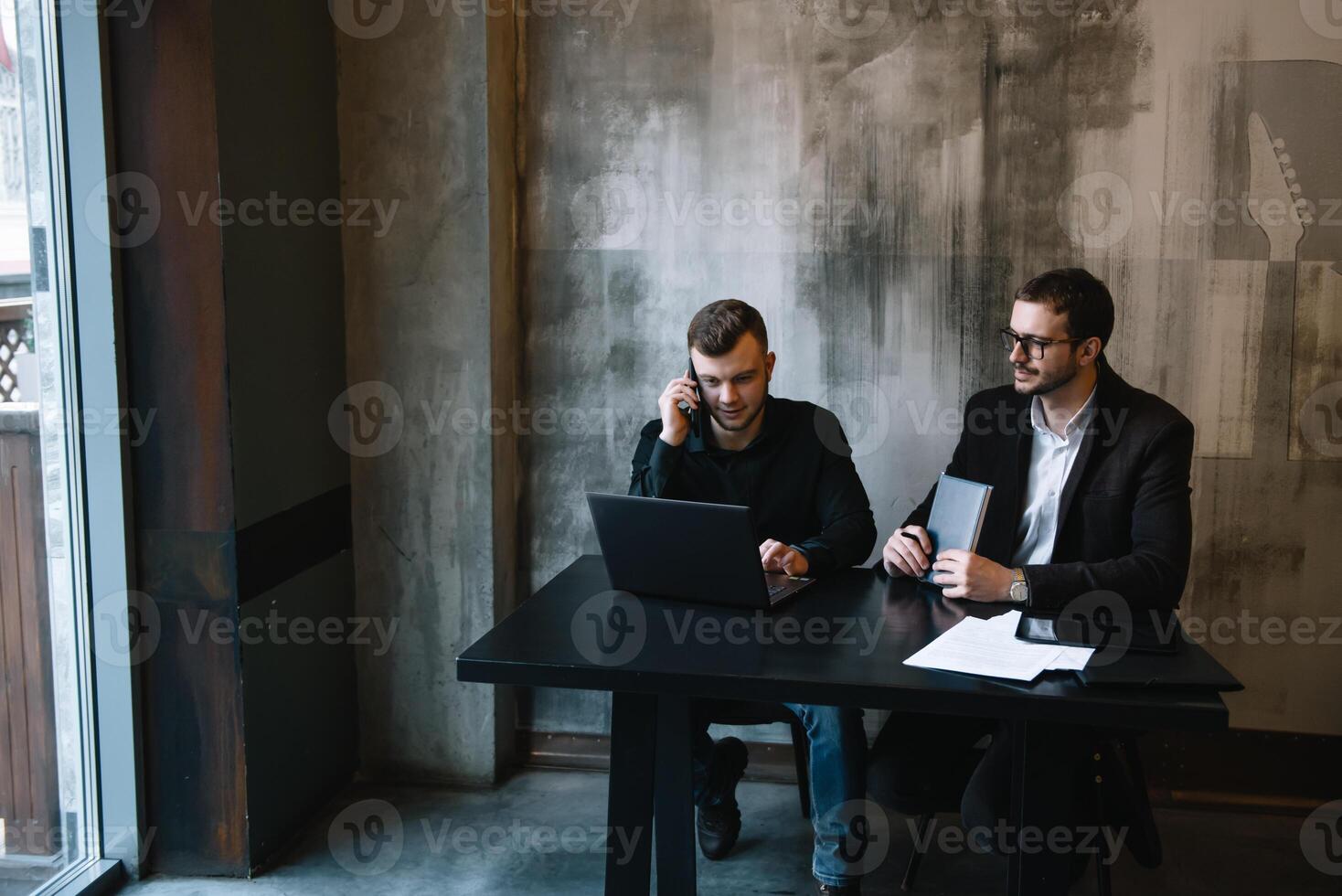 dos empresarios en un oficina sonriente a el cámara mientras trabajando juntos detrás un ordenador portátil computadora. foto