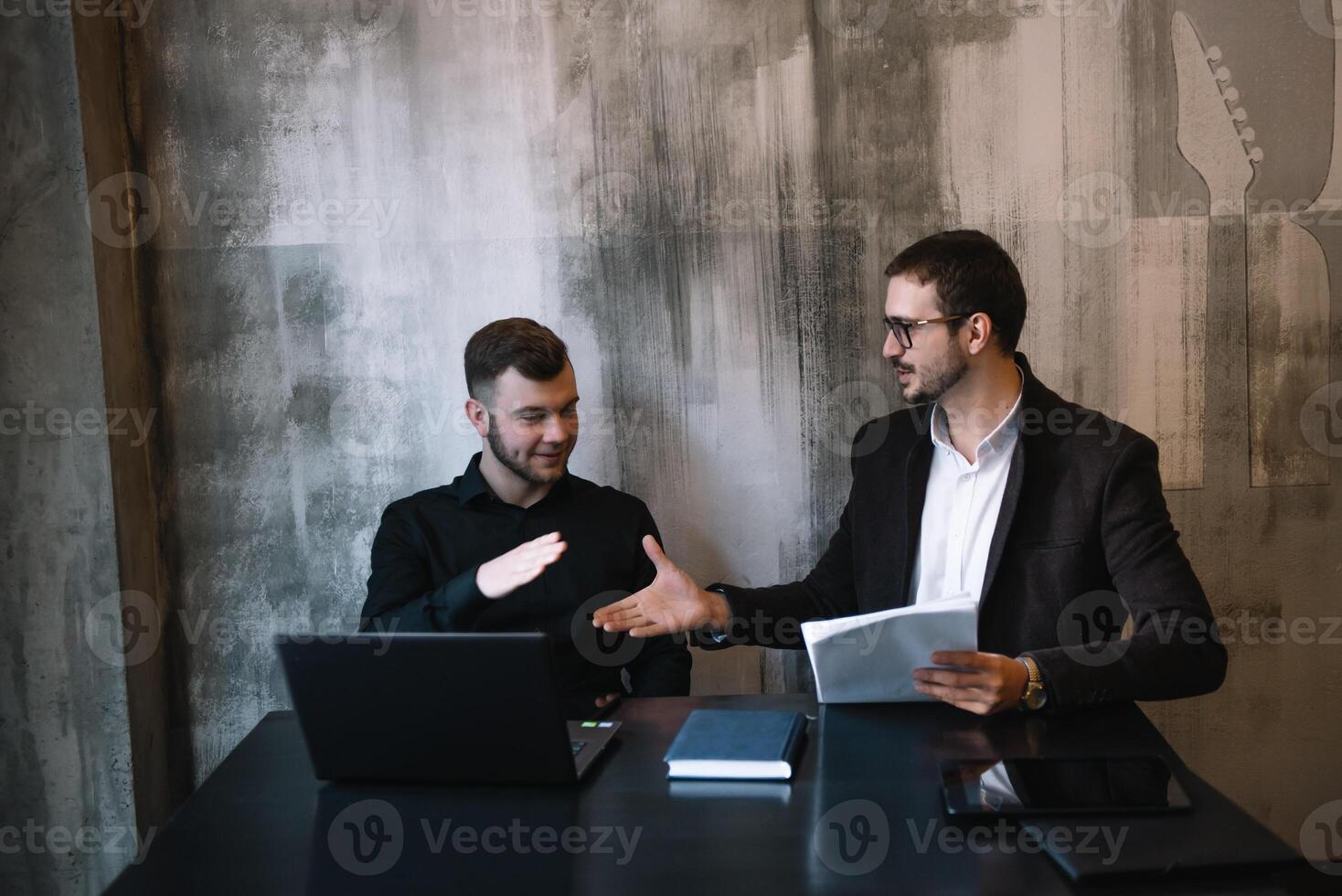 dos empresarios en un oficina sonriente a el cámara mientras trabajando juntos detrás un ordenador portátil computadora. foto