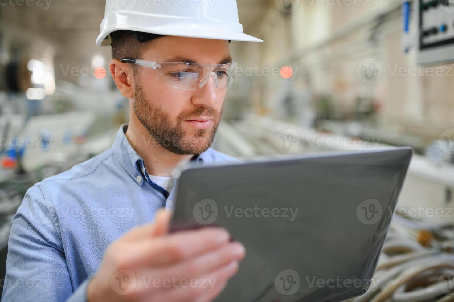 Engineer in hardhat is using a laptop in a heavy industry factory photo