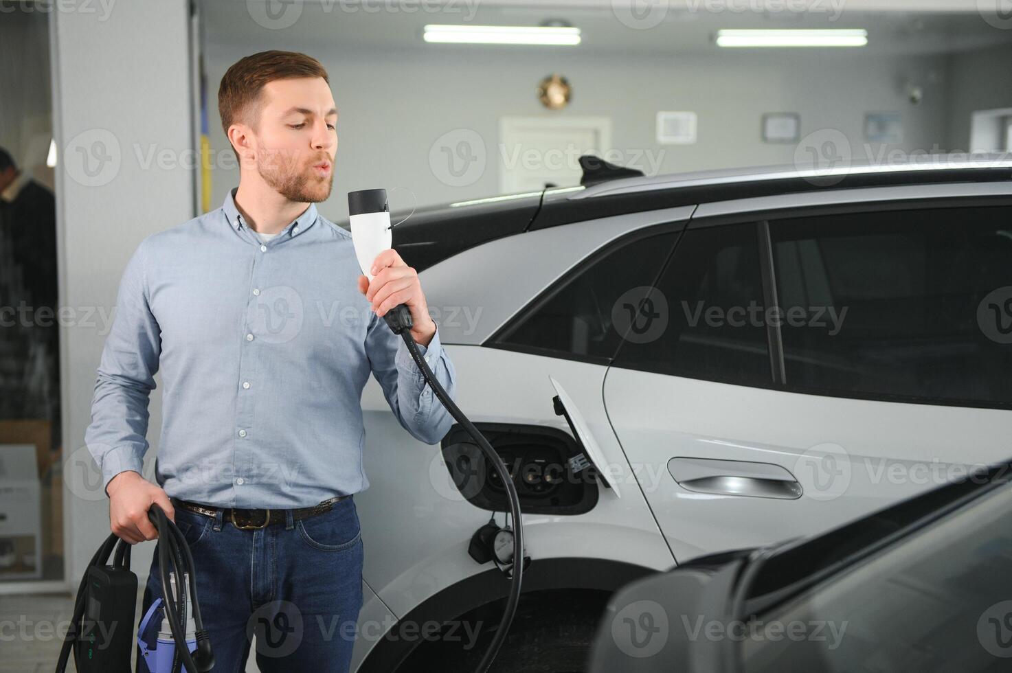 Beard man trying a new charging cable with a car charging station at the motor dealership. Concept of buying electric vehicle. Smart ecological living photo
