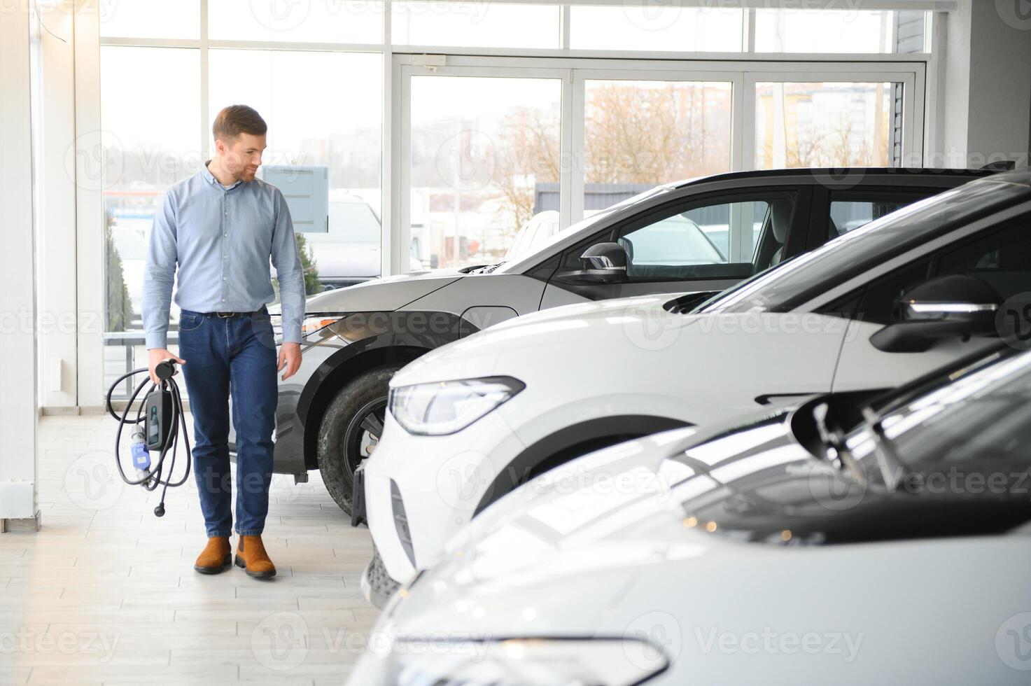 concepto de comprando eléctrico vehículo. hermoso negocio hombre soportes cerca eléctrico coche a concesión foto