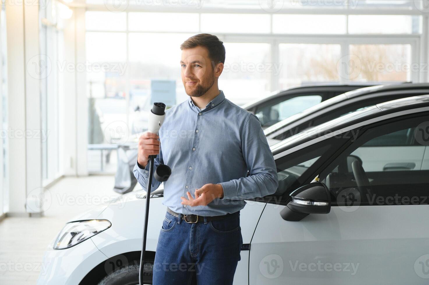 joven hombre, de venta eléctrico carros en el sala de exposición. concepto de comprando Respetuoso del medio ambiente coche para familia foto