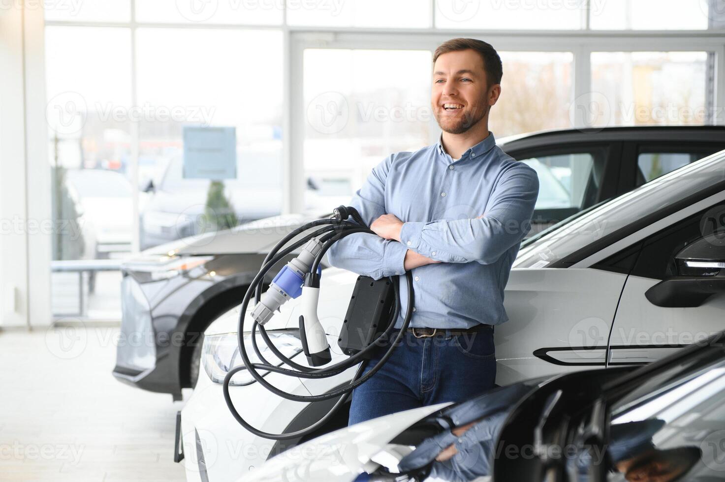 Beard man trying a new charging cable with a car charging station at the motor dealership. Concept of buying electric vehicle. Smart ecological living photo