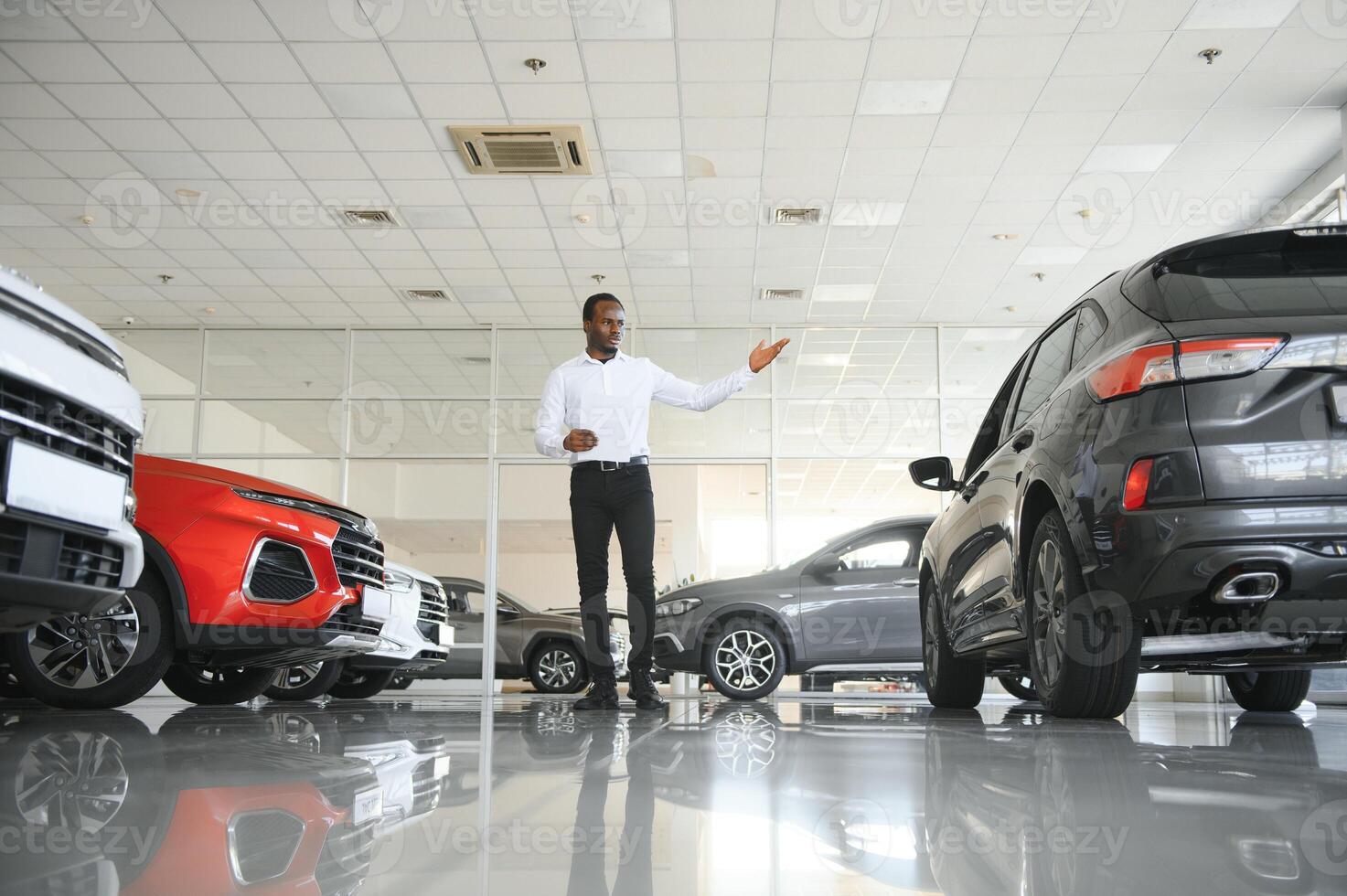 Cars Dealership Concept. Auto Seller Afro Man Standing In Automobile Center photo