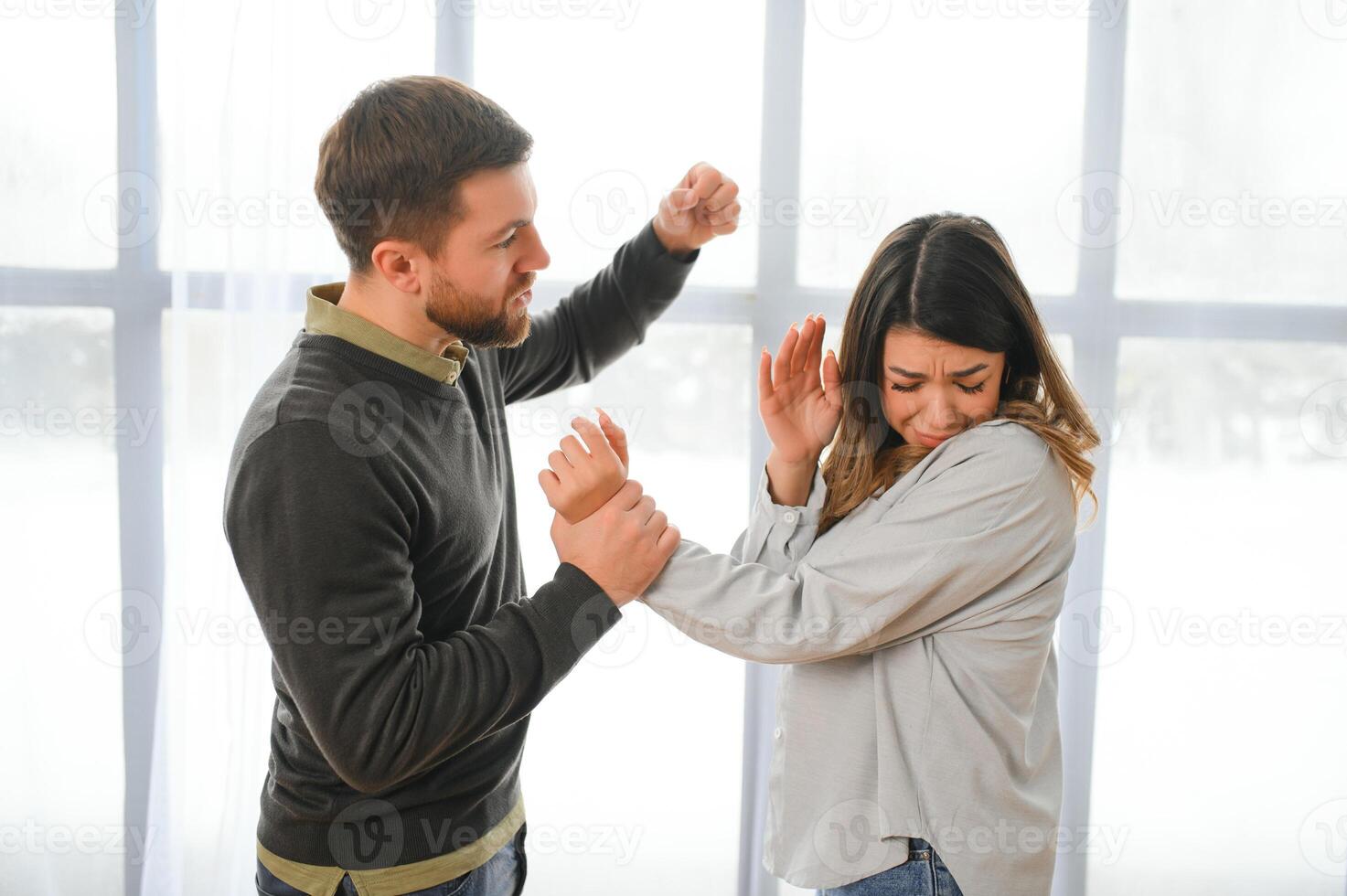 Quarrel, violence and husband beats wife at home. Angry man raises his fist at frightened woman. photo